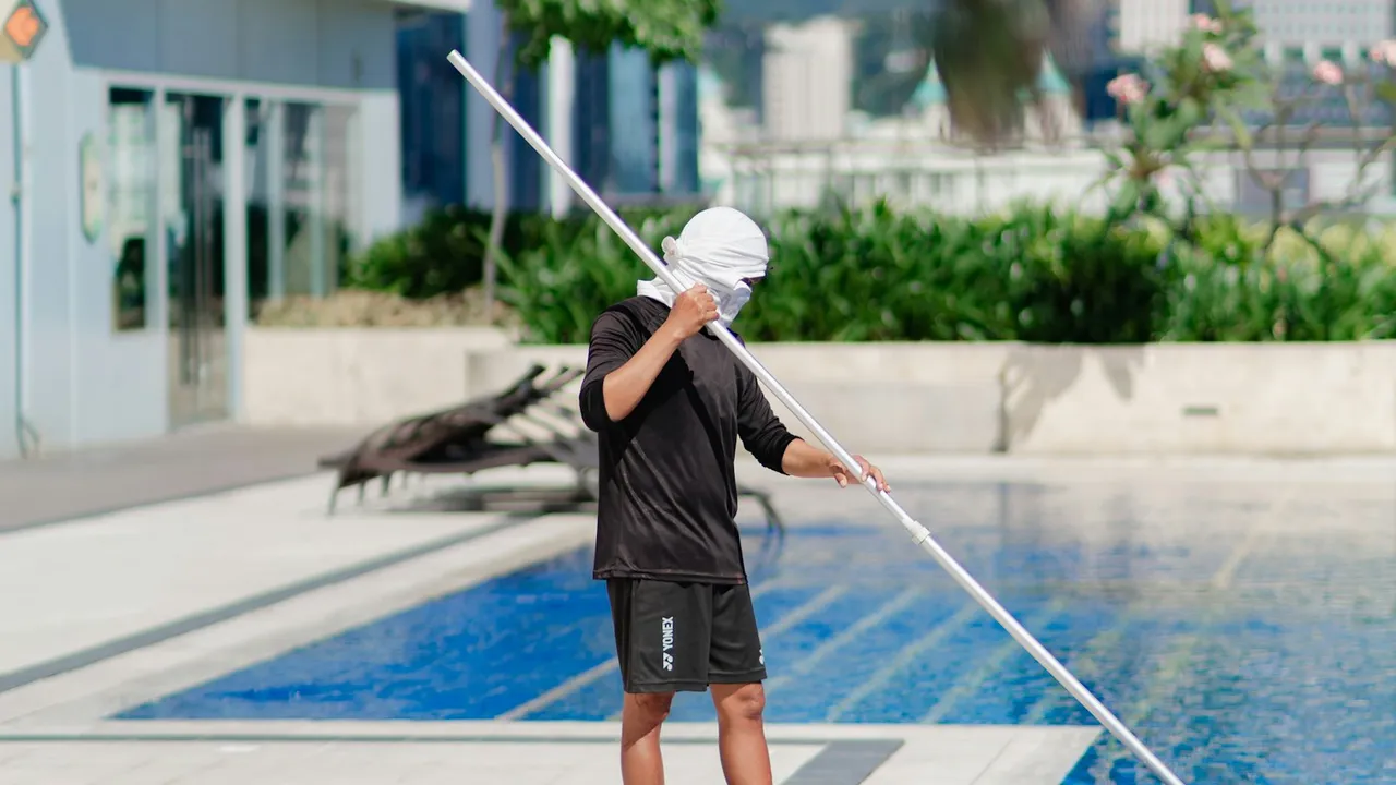 A pool technician cleaning a swimming pool with a long pole