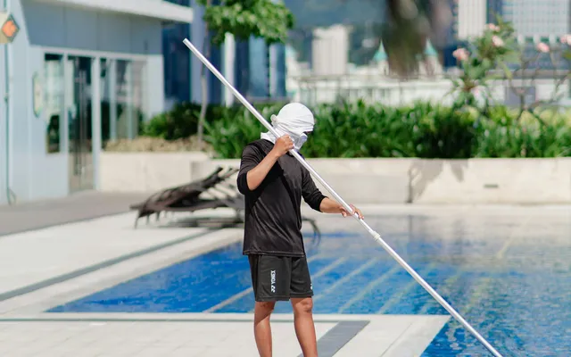 A pool technician cleaning a swimming pool with a long pole